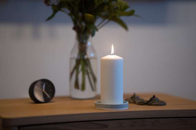 Ett tänt ljus i mörker, med lugnt bokeh-ljus i bakgrunden
